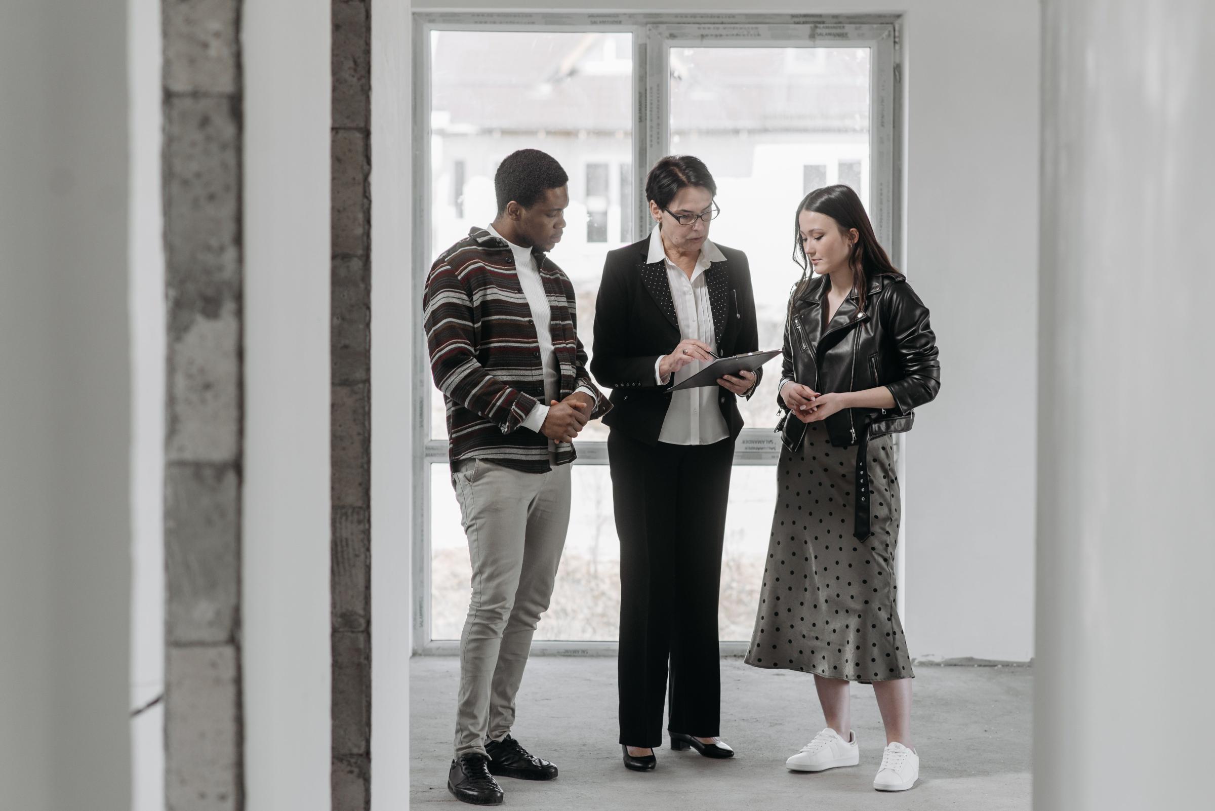 Real estate agent reviewing a clipboard with a young couple in an empty room